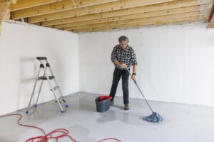 A man is mopping the concrete floor of an unfinished basement in South Kansas City.